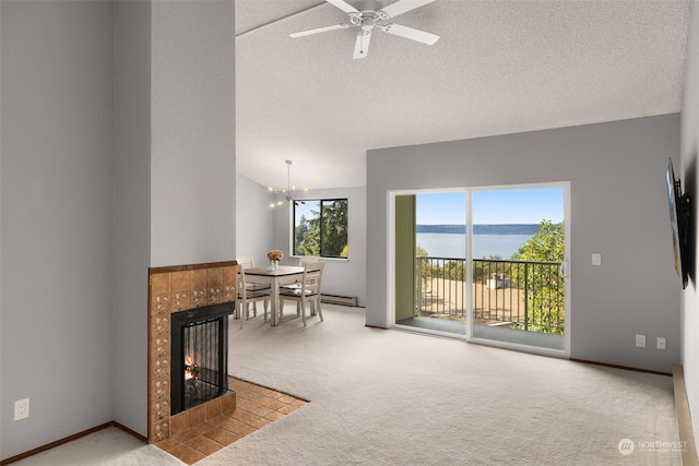 carpeted living room featuring a baseboard heating unit, a tiled fireplace, a textured ceiling, ceiling fan with notable chandelier, and a water view