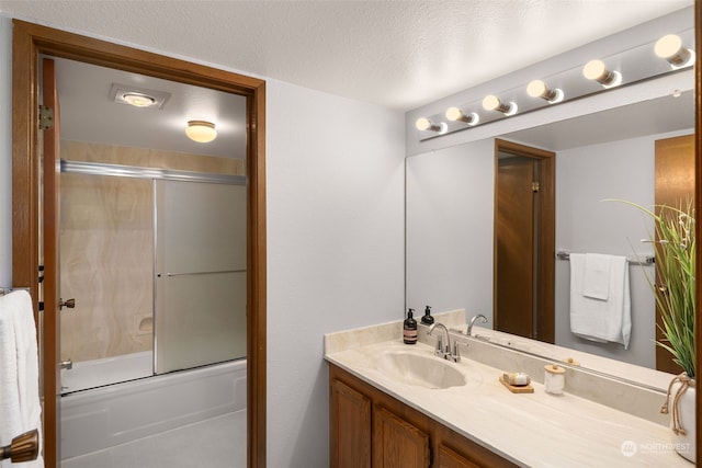 bathroom with bath / shower combo with glass door, a textured ceiling, and vanity