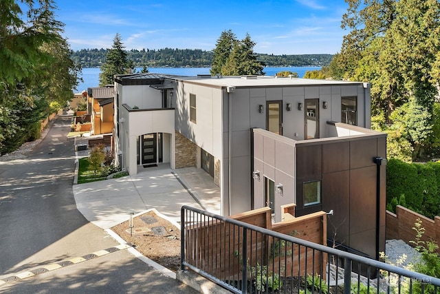 contemporary house featuring concrete driveway, stone siding, an attached garage, a water view, and fence
