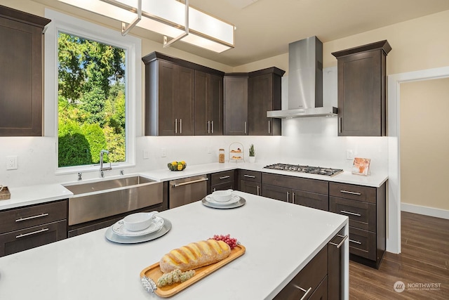 kitchen featuring wall chimney range hood, dark brown cabinetry, stainless steel gas stovetop, and a sink