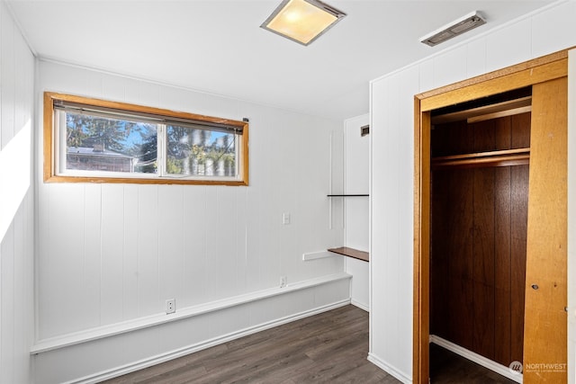 unfurnished bedroom with wooden walls, a closet, and dark wood-type flooring