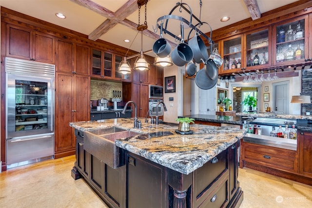 kitchen with pendant lighting, light stone counters, beverage cooler, beam ceiling, and a center island with sink