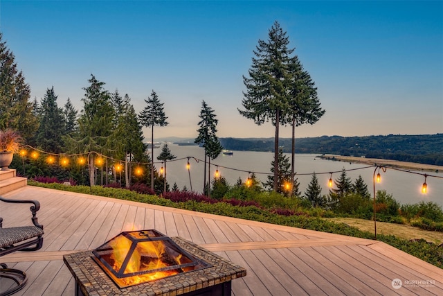 deck at dusk featuring a water view and an outdoor fire pit