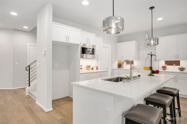 kitchen with white cabinets, stainless steel microwave, a center island with sink, and hanging light fixtures