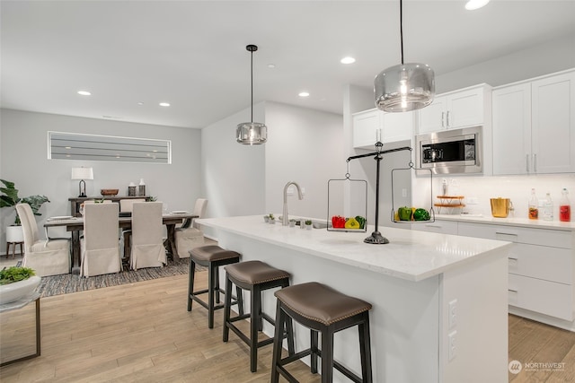 kitchen featuring white cabinetry, stainless steel microwave, and an island with sink