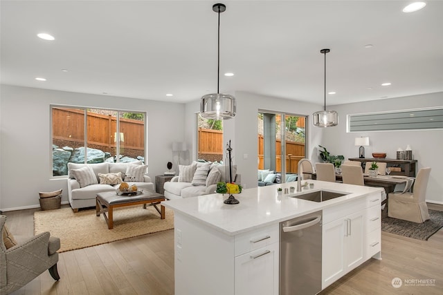 kitchen featuring pendant lighting, white cabinets, an island with sink, sink, and stainless steel dishwasher