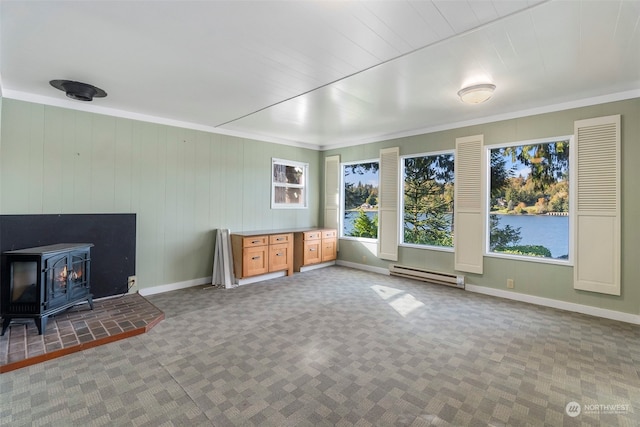 unfurnished living room with wooden walls, a wood stove, a baseboard heating unit, ornamental molding, and carpet flooring