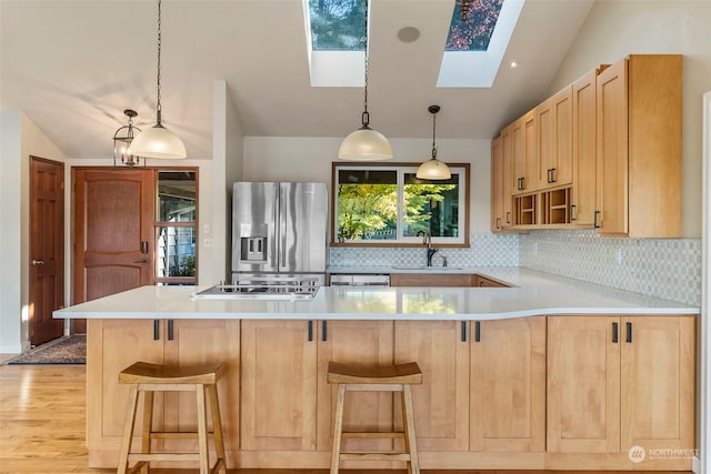 kitchen featuring vaulted ceiling with skylight, backsplash, appliances with stainless steel finishes, light brown cabinetry, and light wood-type flooring