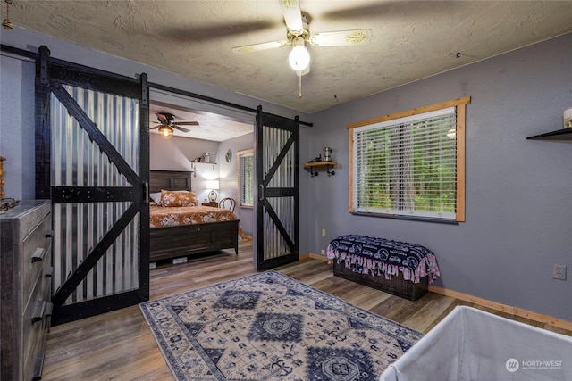 bedroom with ceiling fan, a textured ceiling, a barn door, and wood-type flooring