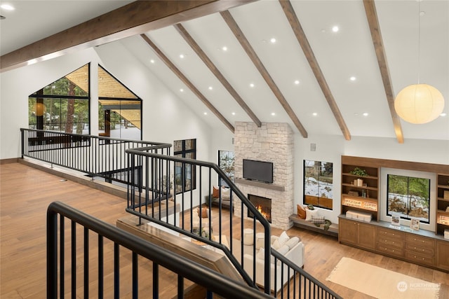 interior space with beamed ceiling, hardwood / wood-style flooring, a stone fireplace, and high vaulted ceiling