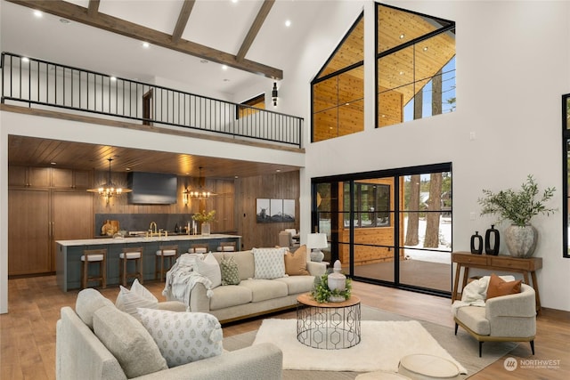 living room with light hardwood / wood-style flooring, high vaulted ceiling, a notable chandelier, beamed ceiling, and wood walls