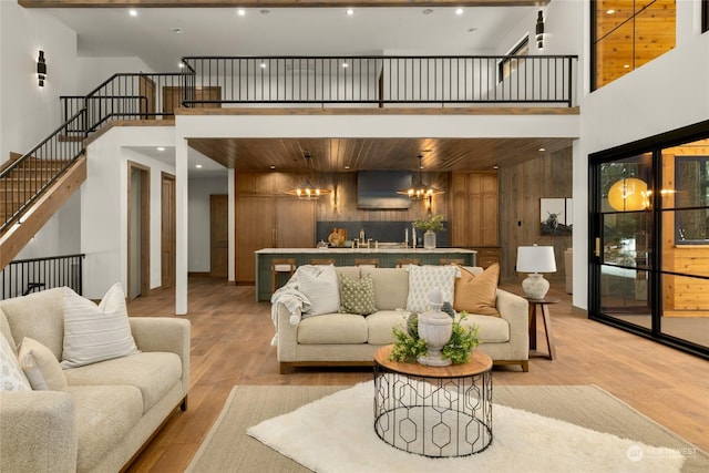 living room featuring wood walls, sink, a towering ceiling, light hardwood / wood-style floors, and a chandelier