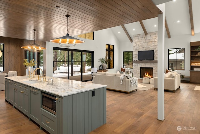 kitchen with pendant lighting, sink, built in microwave, an island with sink, and light stone counters