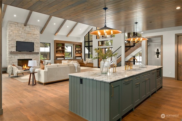 kitchen featuring light stone counters, a notable chandelier, a stone fireplace, hanging light fixtures, and an island with sink