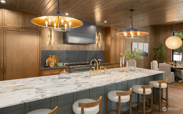 kitchen with light stone countertops, extractor fan, sink, decorative light fixtures, and hardwood / wood-style floors