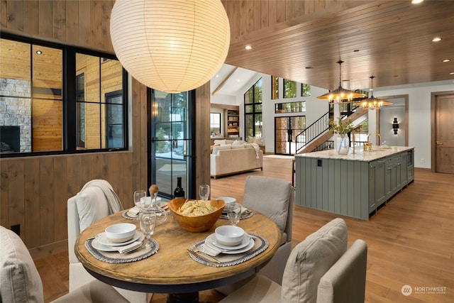 dining room featuring wood ceiling, sink, light hardwood / wood-style floors, a stone fireplace, and wood walls