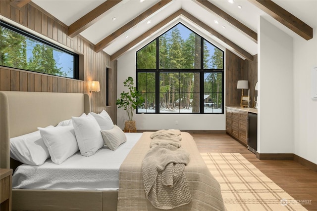 bedroom featuring beam ceiling, light wood-type flooring, high vaulted ceiling, and wooden walls