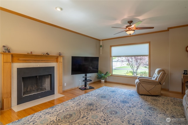 living room with ceiling fan, ornamental molding, a tiled fireplace, and light hardwood / wood-style floors