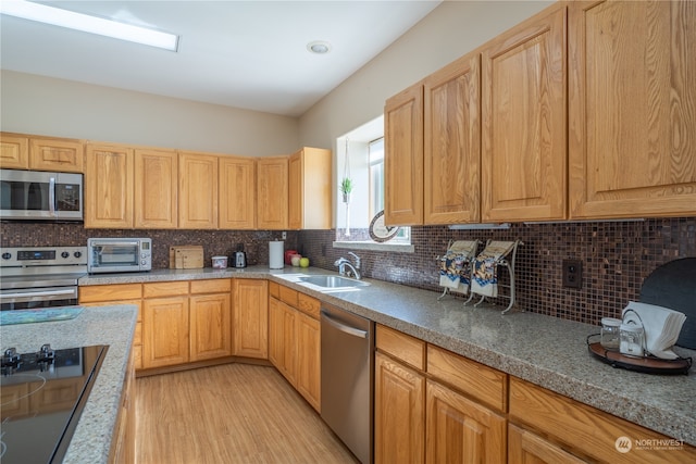 kitchen with appliances with stainless steel finishes, decorative backsplash, light brown cabinets, light wood-type flooring, and sink