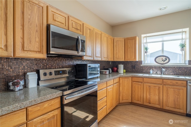 kitchen featuring appliances with stainless steel finishes, light stone counters, tasteful backsplash, light hardwood / wood-style flooring, and sink