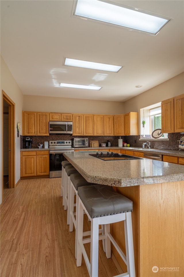 kitchen featuring appliances with stainless steel finishes, decorative backsplash, light hardwood / wood-style floors, and a kitchen breakfast bar