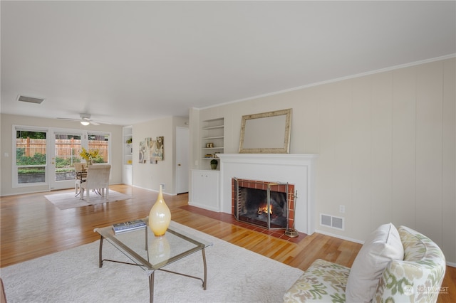 living room featuring ceiling fan, light hardwood / wood-style floors, a fireplace, ornamental molding, and built in shelves