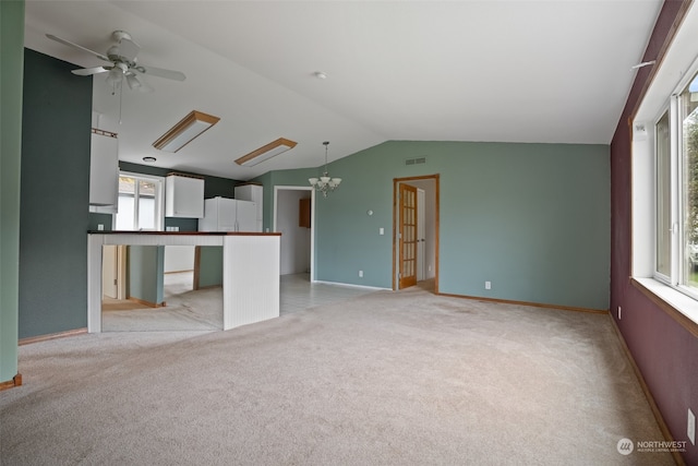 unfurnished living room featuring ceiling fan with notable chandelier, lofted ceiling, a wealth of natural light, and light colored carpet