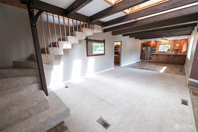 unfurnished living room with carpet floors, beam ceiling, and sink