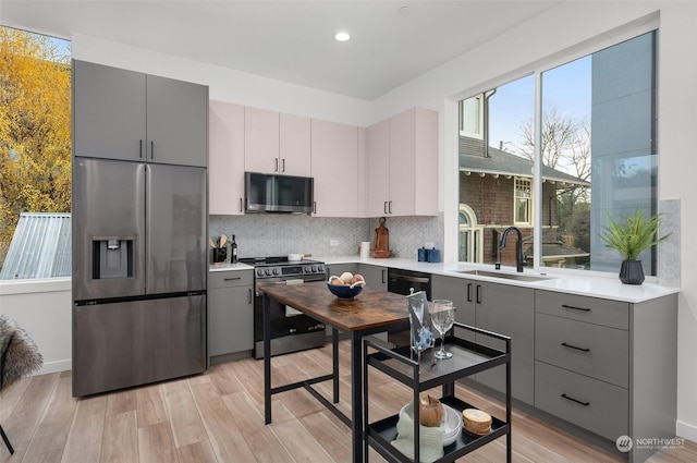 kitchen with gray cabinetry, stainless steel appliances, light hardwood / wood-style floors, and sink