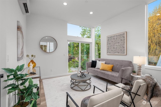 living room with a wall mounted air conditioner, a healthy amount of sunlight, and light wood-type flooring