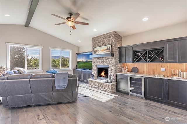 living room featuring vaulted ceiling with beams, a fireplace, wine cooler, light wood-type flooring, and ceiling fan