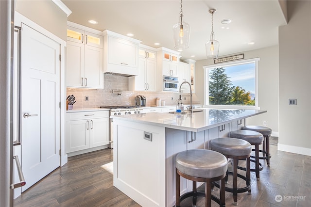 kitchen featuring stainless steel appliances, dark wood-type flooring, white cabinets, a kitchen island with sink, and decorative light fixtures