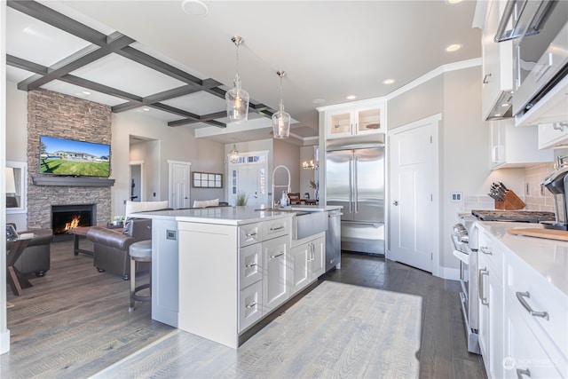 kitchen with premium appliances, white cabinetry, a center island with sink, and coffered ceiling