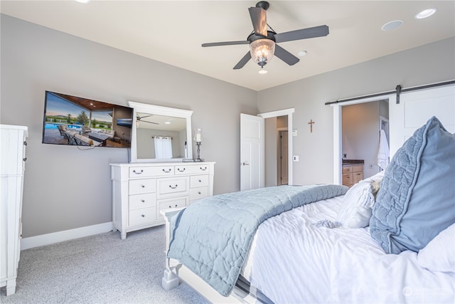 carpeted bedroom with connected bathroom, a barn door, and ceiling fan