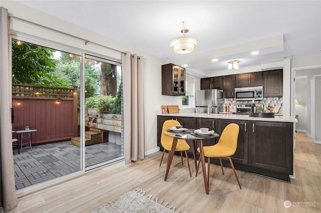 kitchen with decorative backsplash, stainless steel appliances, kitchen peninsula, light hardwood / wood-style flooring, and dark brown cabinets