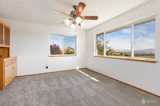 unfurnished room with a mountain view, a textured ceiling, light colored carpet, and ceiling fan