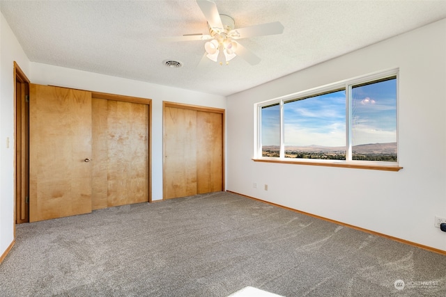 unfurnished bedroom featuring two closets, ceiling fan, carpet floors, and a textured ceiling