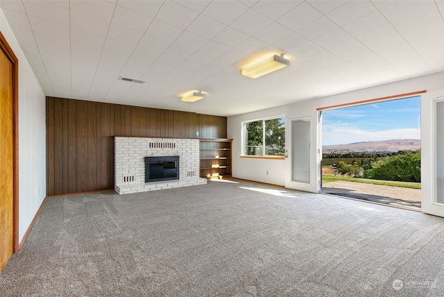 unfurnished living room with carpet, wooden walls, a mountain view, and a fireplace