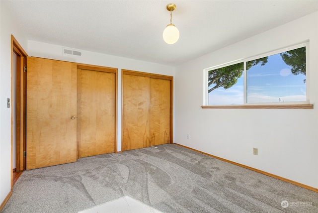 unfurnished bedroom featuring light carpet, a textured ceiling, and two closets