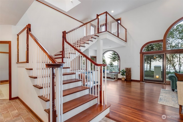 staircase with wood-type flooring, a high ceiling, a wealth of natural light, and a skylight