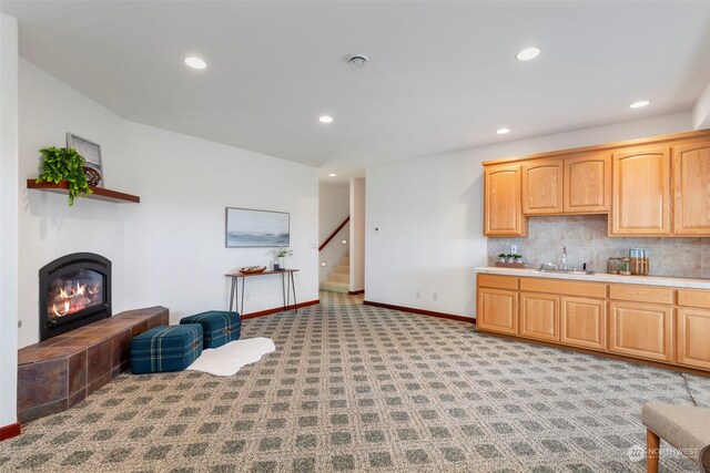 kitchen with backsplash, light colored carpet, sink, light brown cabinets, and a tiled fireplace