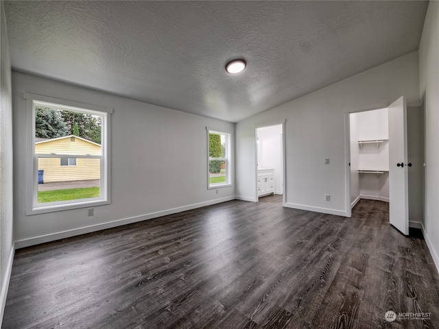 unfurnished bedroom with a textured ceiling, a walk in closet, a closet, dark hardwood / wood-style floors, and vaulted ceiling