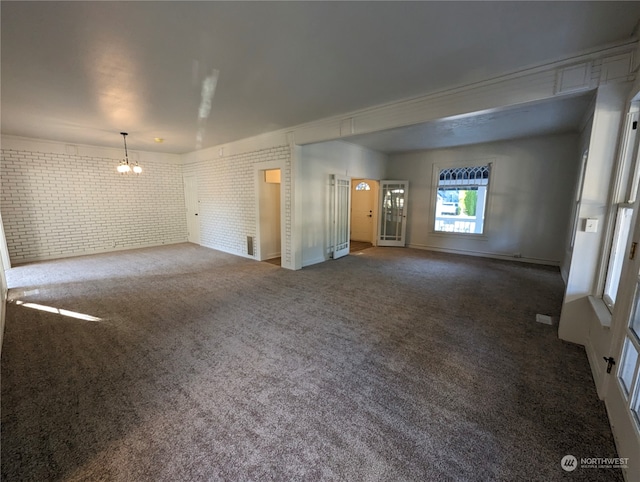 unfurnished living room featuring dark carpet, brick wall, and a chandelier