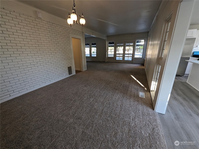 carpeted spare room featuring a chandelier, brick wall, and ornamental molding