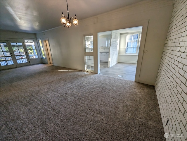 carpeted spare room featuring french doors, ornamental molding, and a notable chandelier