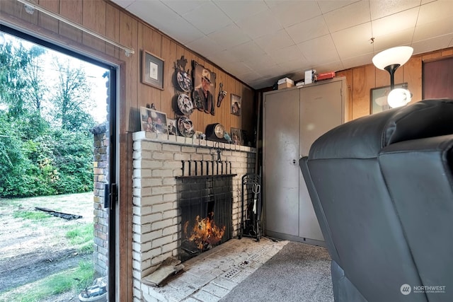 unfurnished living room with a fireplace, wooden walls, and light colored carpet