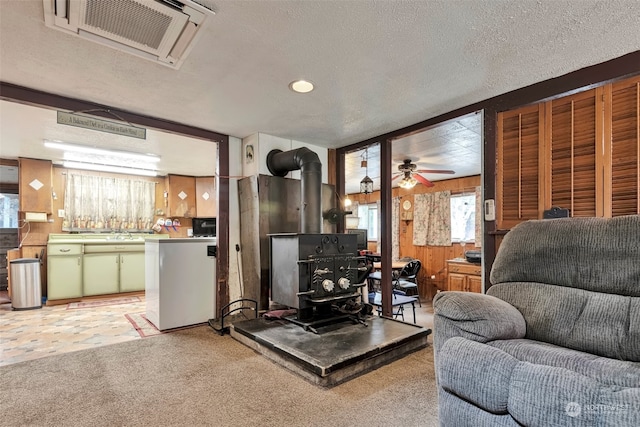 carpeted living room featuring a textured ceiling, wood walls, ceiling fan, and a wood stove