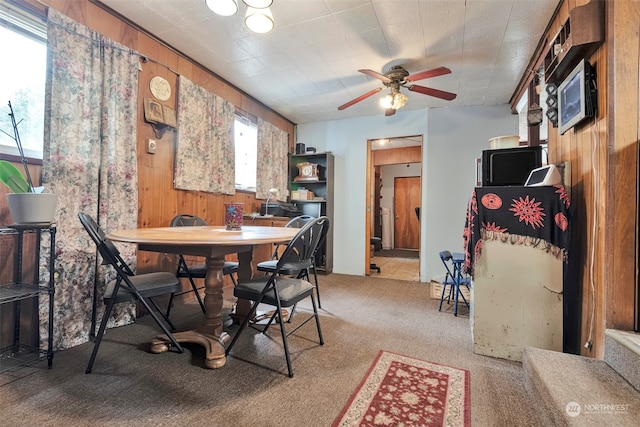 dining area with ceiling fan, wooden walls, plenty of natural light, and carpet flooring