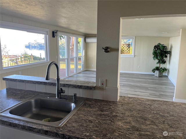 kitchen with a wall mounted air conditioner, sink, light wood-type flooring, and a textured ceiling