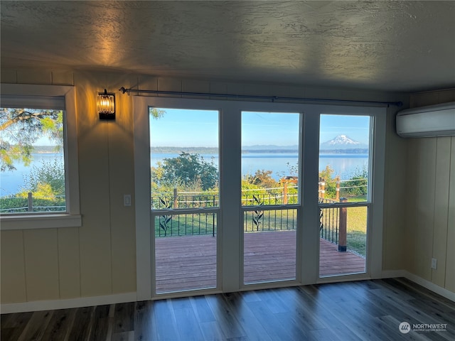 doorway to outside with a wall mounted air conditioner, plenty of natural light, hardwood / wood-style floors, and a water and mountain view